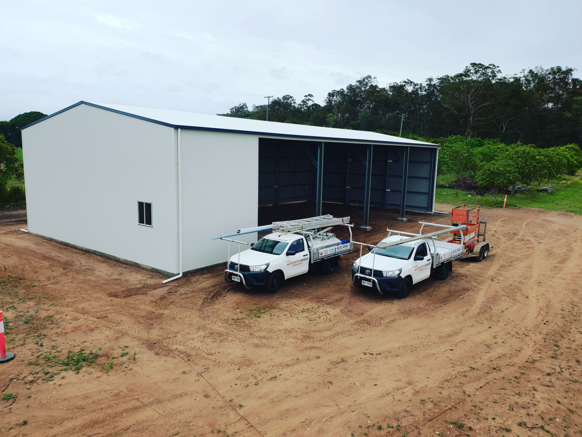 Farm machinery shed with an enclosed workshop bay with roller door, glass sliding door and window at one end and four open machinery bays
