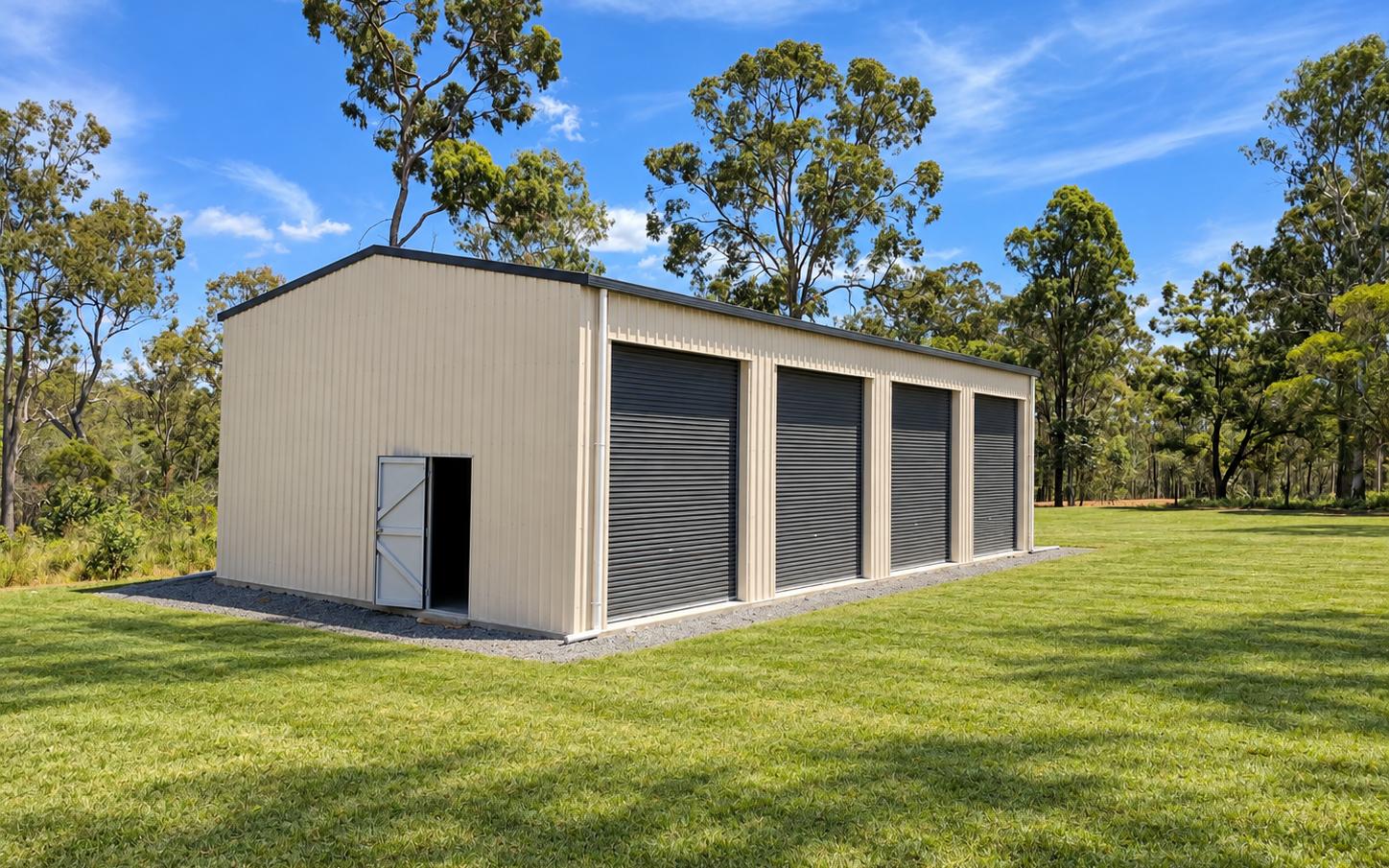Cream COLORBOND four-bay toy shed with dark roller doors, personal access door and window on a grassy rural block