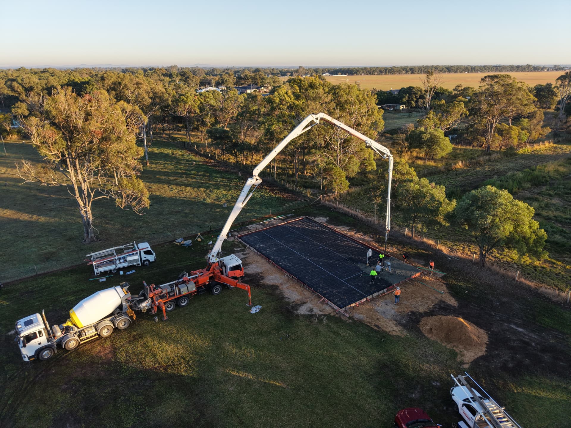 Spartan Sheds™ tradesmen pouring a shed slab on site, with concrete pump and trucks on a rural Wide Bay property