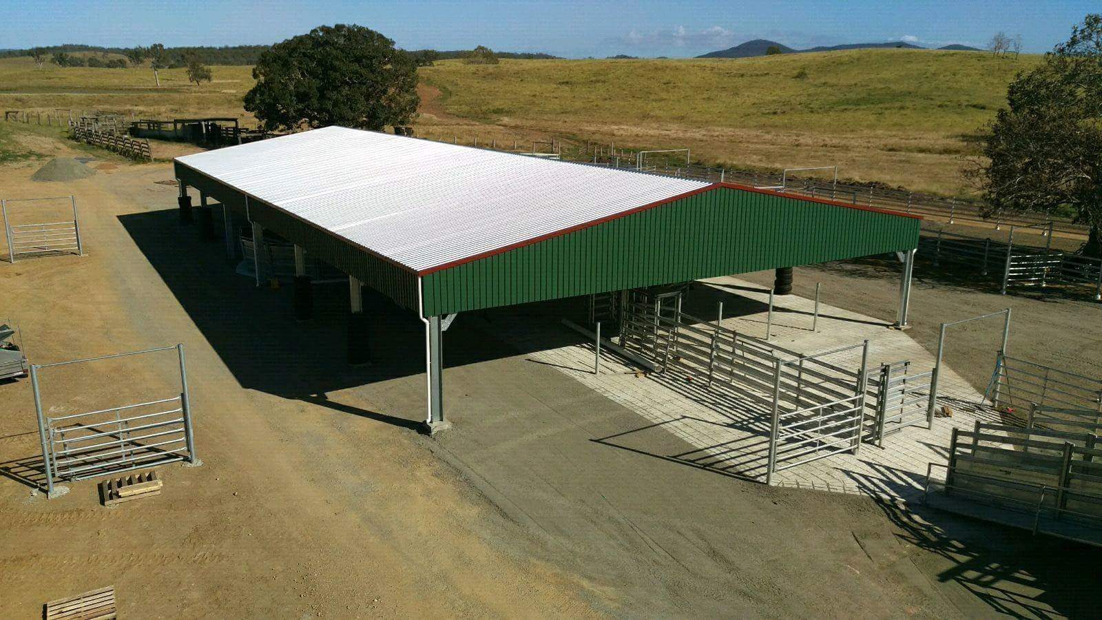 Large green and white open-sided clear-span cattle yard cover with perimeter skirt sheeting on a Queensland property