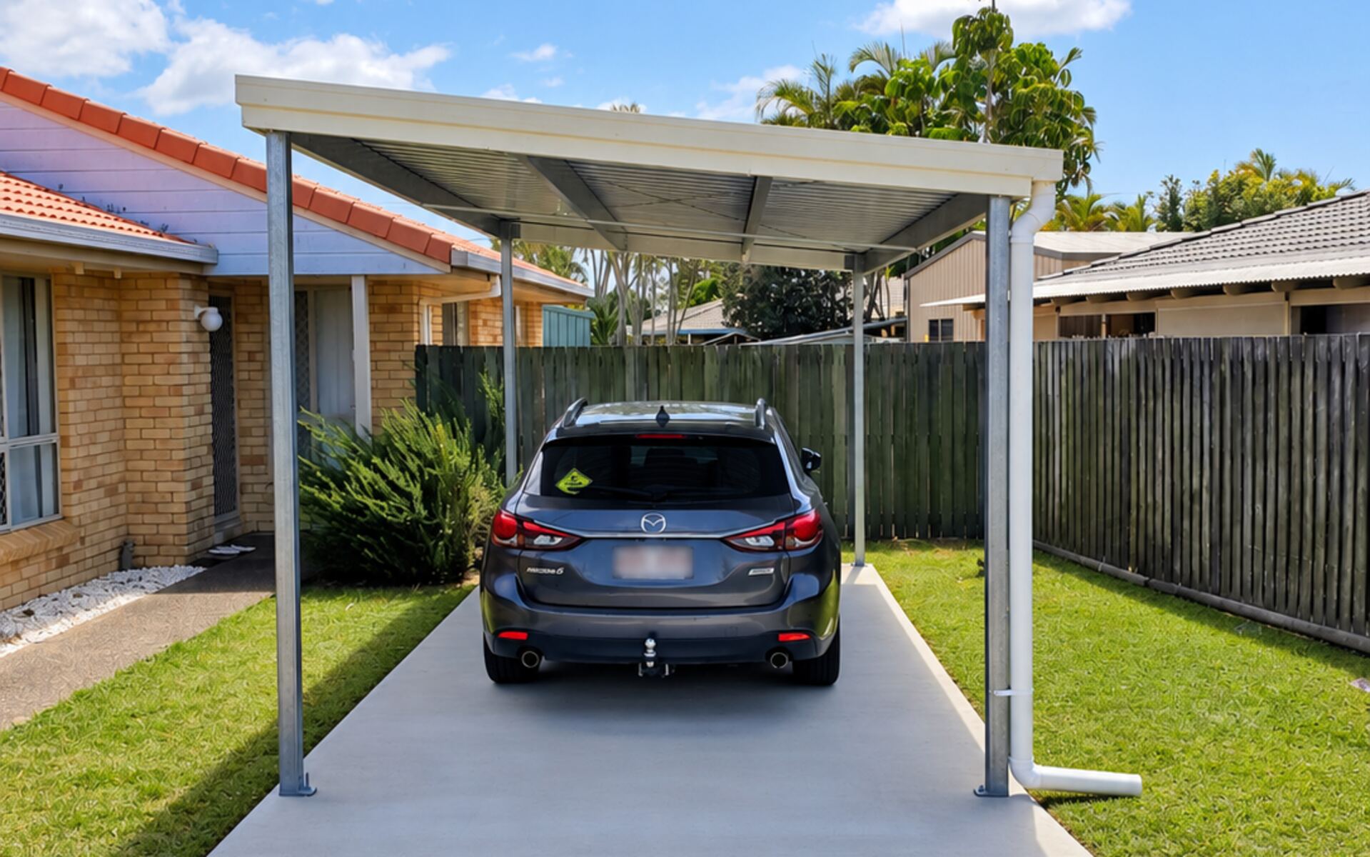 Single steel carport sheltering a family SUV in a Bundaberg backyard, light coloured frame and roof over a concrete driveway