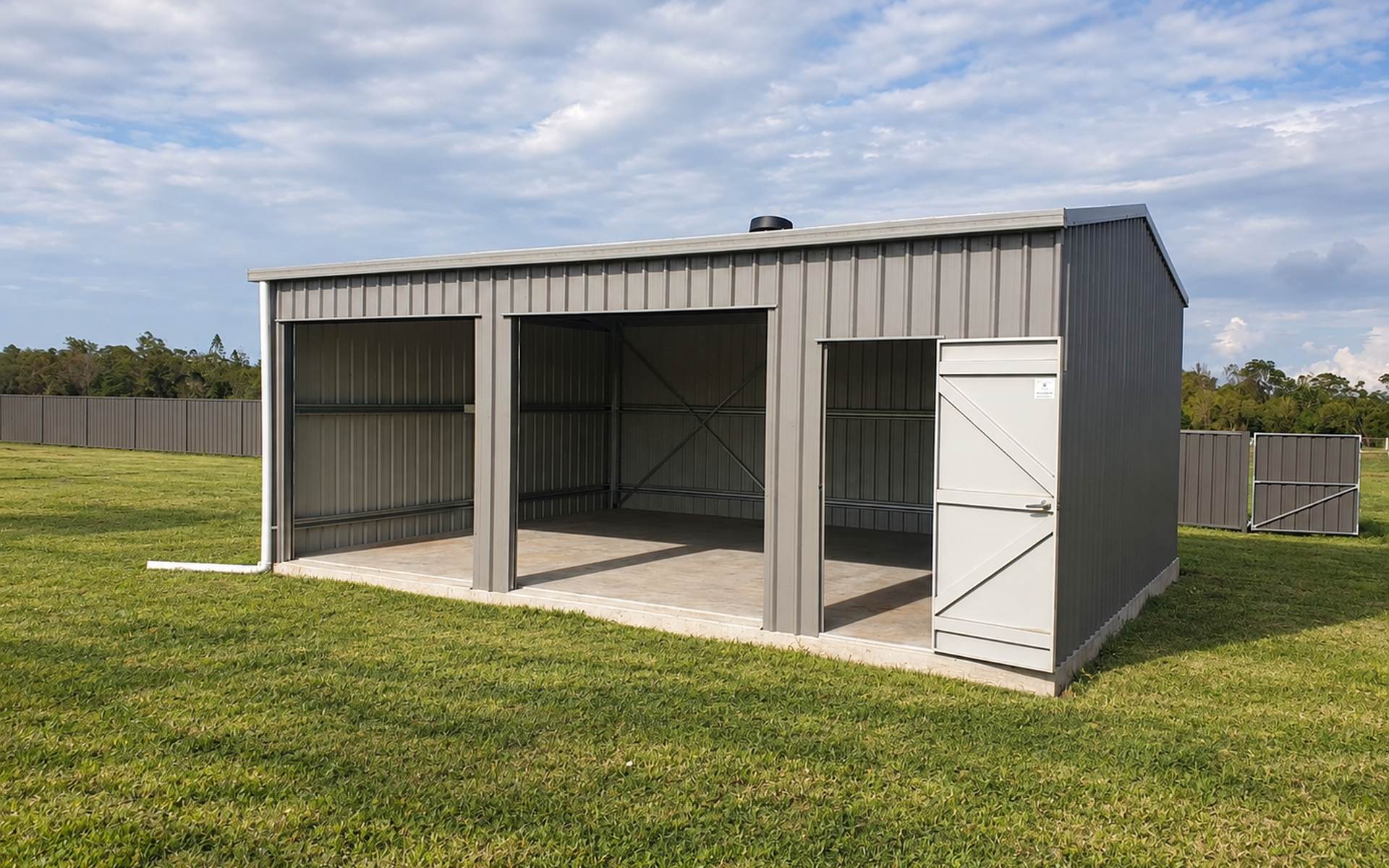 Grey COLORBOND triple garage workshop with two roller door openings and personal access door on a grassy rural block