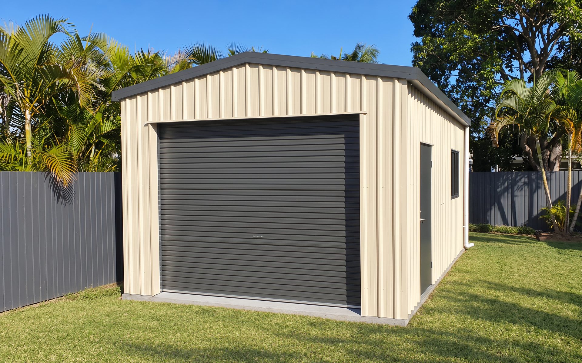 Cream COLORBOND single garage with dark grey roller door, personal access door and window in a Bundaberg backyard