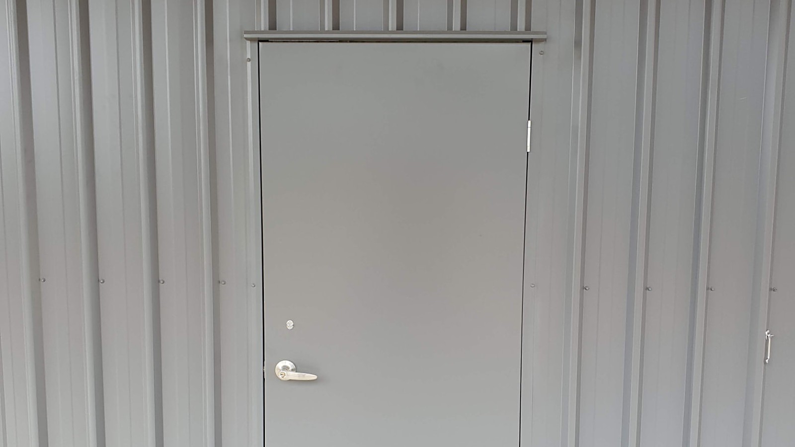 Grey personal access door with head flashing, lever lockset and deadlock fitted to a COLORBOND steel shed wall by Spartan Sheds in Bundaberg QLD