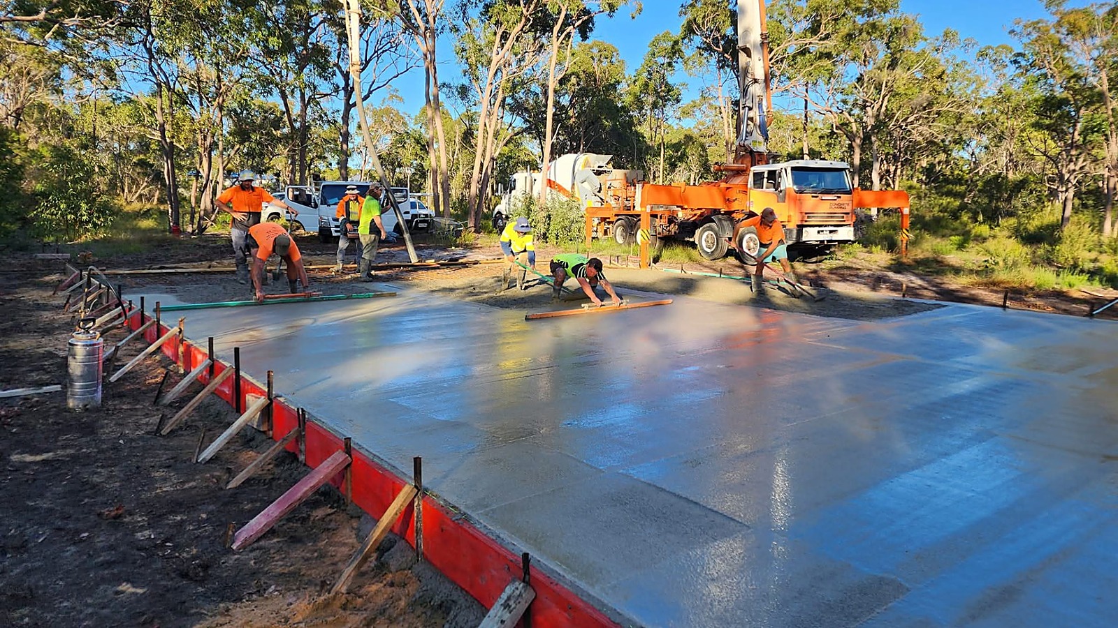 Concreting crew screeding a freshly poured engineered shed slab with a concrete pump and agitator on site in the Bundaberg region