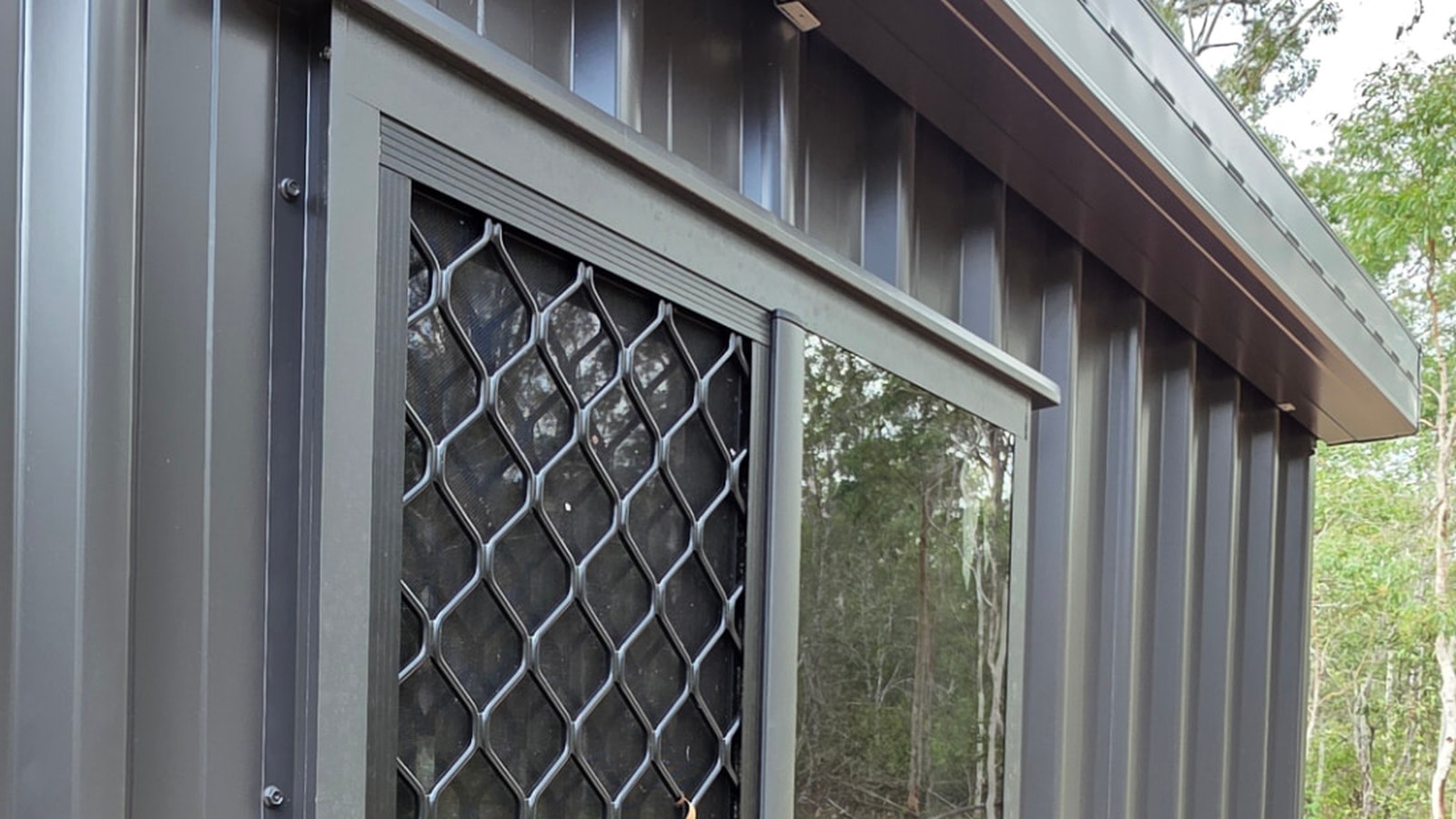 Aluminium sliding window with security mesh and head flashing fitted to a charcoal COLORBOND steel shed wall by Spartan Sheds in Bundaberg QLD